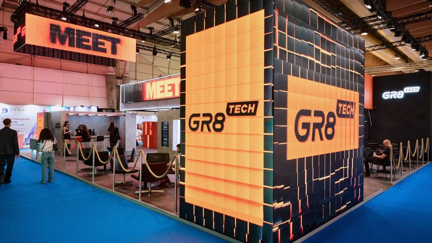 GR8 Tech exhibition stand at an iGaming trade show with large LED cube displaying the company name, seating area and blue carpet